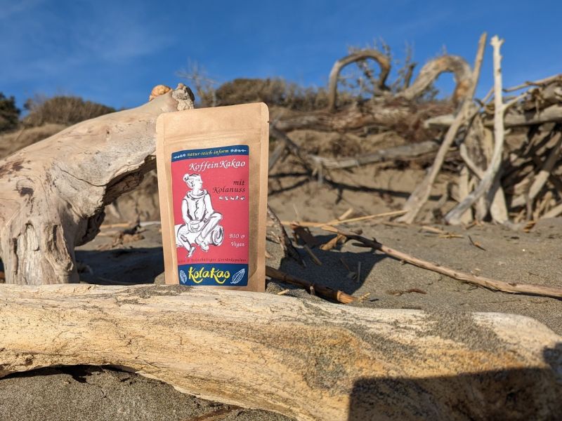 KolaKao der KoffeinKakao mit Kolanuss, zwischen Schwemmholz in der Dünenlandschaft am Mittelmeer. neu und endlich pur, nur Kolanuss und Kakao, leicht gesüßt.  Die Neuheit 2023 aus der Getränkepulver-Manufaktur natur-reich-inform.
